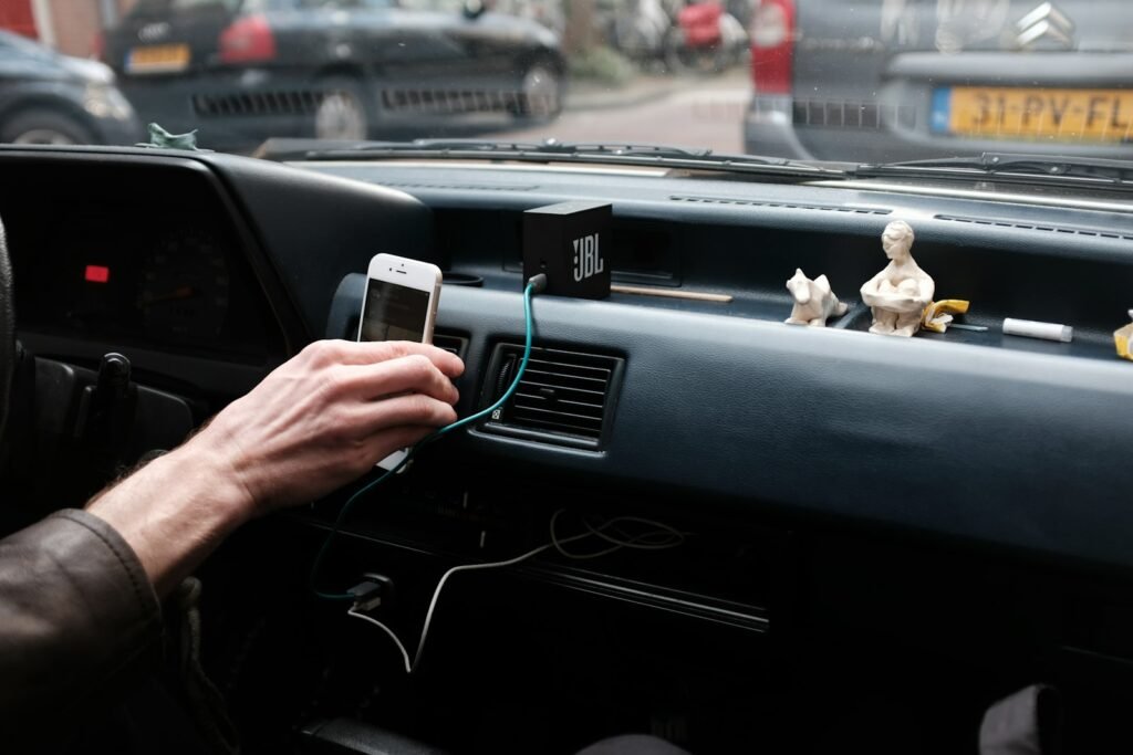 Hand holding an iPhone above a car dashboard during the day