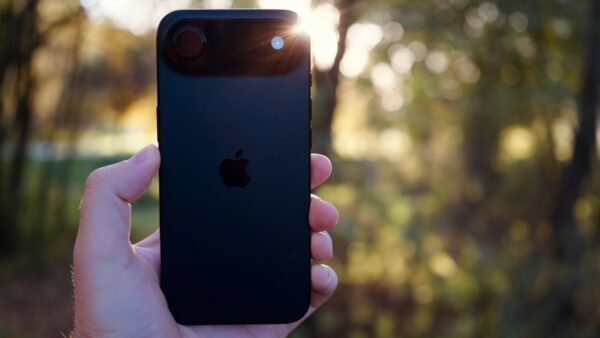 Hand holding a black smartphone in bright sunlight with sun flare